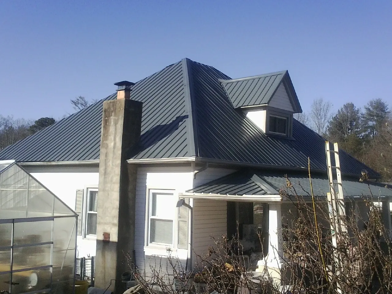 Dark blue standing seam metal roof on a white farmhouse with dormer — Slate & Tile Roof Repair by Roofing Brothers in Interlaken