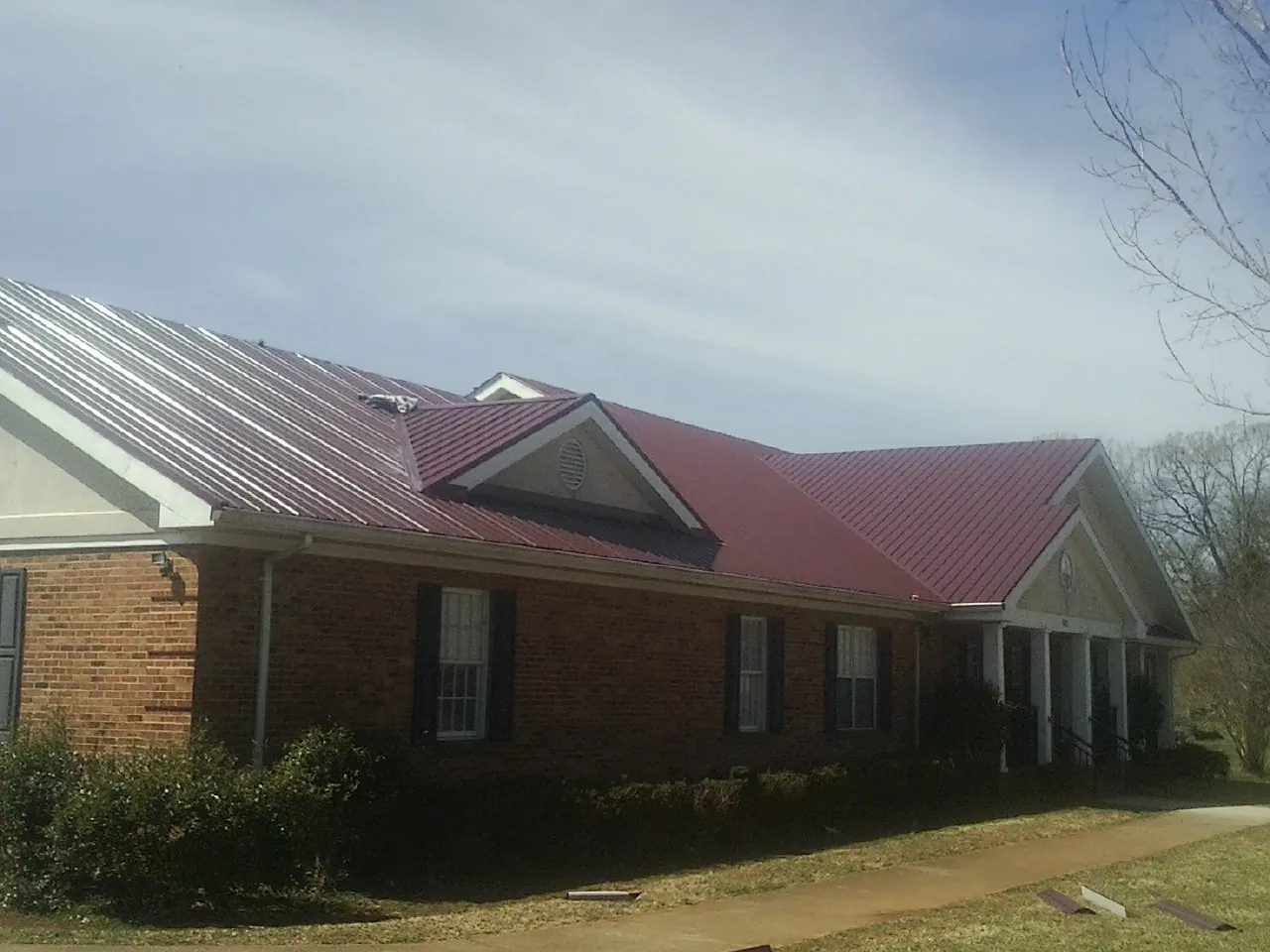 Red metal roof with gabled entries on a long brick building, from a Hail Damage Roof Repair job in Interlaken
