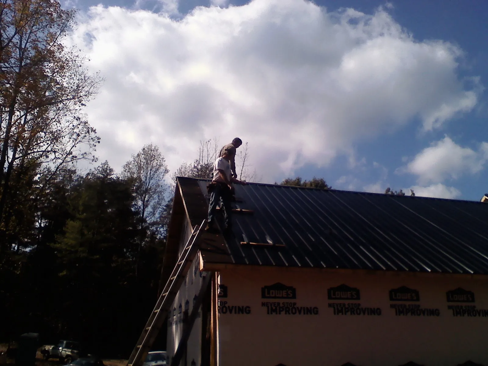 Roofer fastening dark metal panels high against a cloudy sky, from a Roof Inspection job in Interlaken