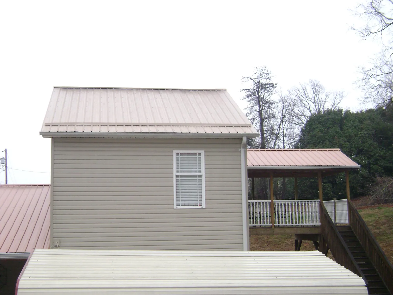 Tan metal roofs on a two story addition and attached porch, from a Roof Replacement job in Interlaken